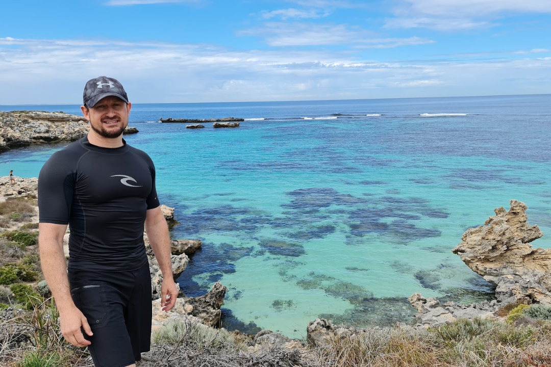 Man wearing baseball cap standing on the shore at Rottnest Island.